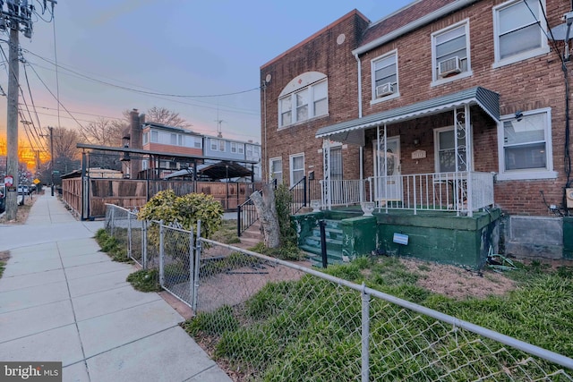 townhome / multi-family property featuring a porch, cooling unit, brick siding, and a fenced front yard