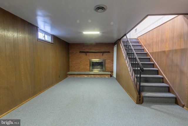 basement with wooden walls, visible vents, stairway, carpet floors, and a fireplace