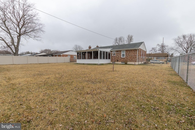 rear view of house featuring brick siding, a sunroom, a chimney, a yard, and a fenced backyard