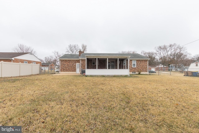 rear view of property with fence, a yard, a sunroom, a chimney, and brick siding