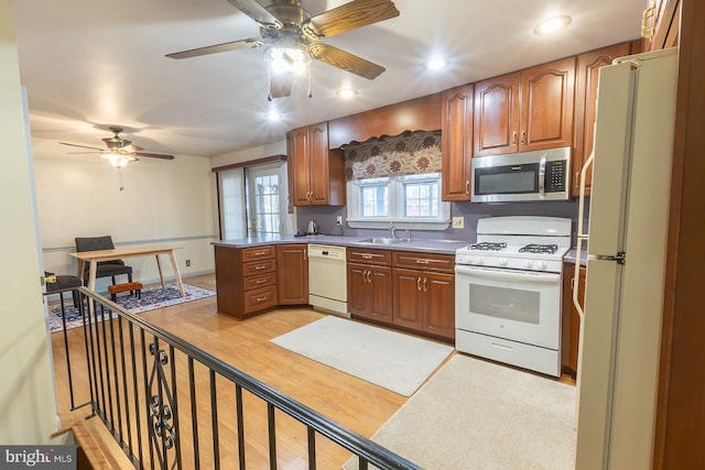 kitchen featuring white appliances, a ceiling fan, a peninsula, a sink, and light wood-style floors