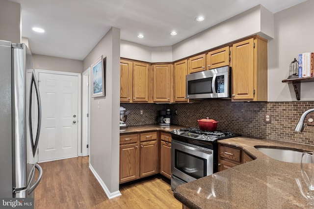 kitchen with a sink, dark stone countertops, appliances with stainless steel finishes, light wood finished floors, and decorative backsplash