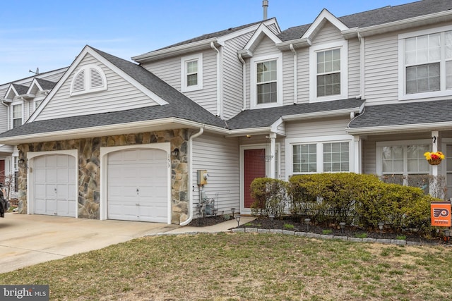 view of front of home featuring driveway, stone siding, a shingled roof, a front yard, and an attached garage