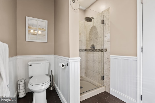 full bathroom with a wainscoted wall, toilet, wood finished floors, and a shower stall