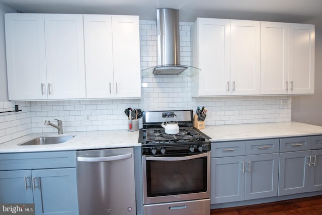 kitchen with a sink, appliances with stainless steel finishes, white cabinetry, wall chimney range hood, and tasteful backsplash