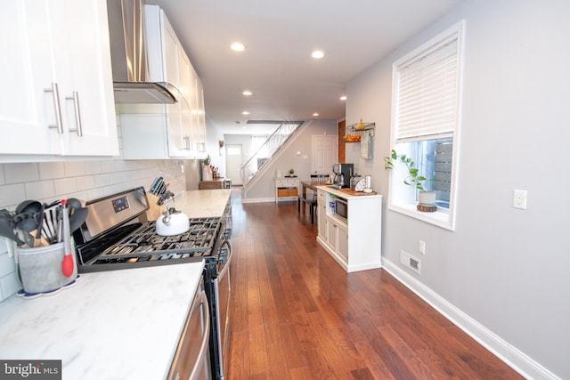 kitchen featuring white cabinetry, backsplash, stainless steel range with gas stovetop, and wall chimney range hood