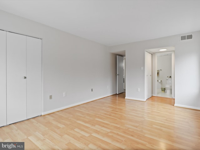 unfurnished bedroom with ensuite bath, visible vents, baseboards, and light wood-style floors