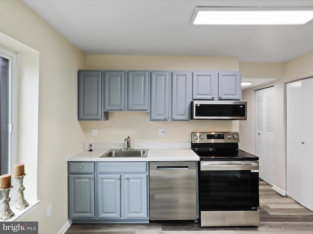 kitchen with blue cabinets, a sink, stainless steel appliances, light wood-style floors, and light countertops