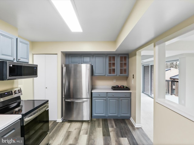 kitchen with glass insert cabinets, light countertops, gray cabinets, appliances with stainless steel finishes, and wood finished floors