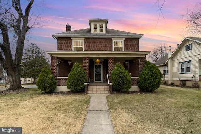 traditional style home with a porch, a yard, brick siding, and a chimney