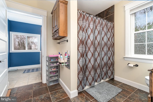 full bathroom featuring a shower with shower curtain, baseboards, and stone tile flooring