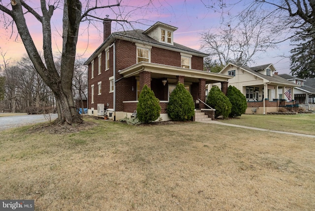 traditional style home featuring a yard, brick siding, a porch, and a chimney