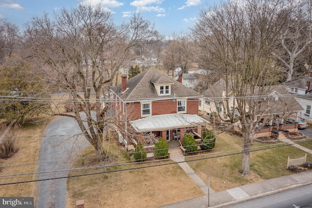 traditional style home featuring a front yard, a porch, a chimney, a fenced front yard, and brick siding