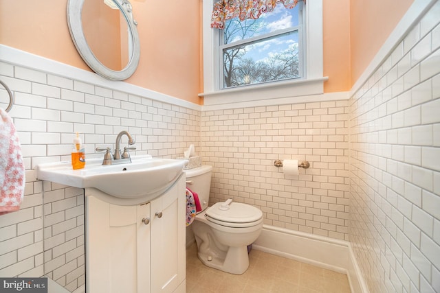 half bathroom featuring tile patterned flooring, tile walls, toilet, wainscoting, and vanity