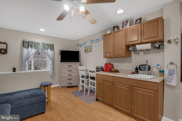 kitchen featuring baseboards, light wood-style flooring, a sink, ceiling fan, and light countertops