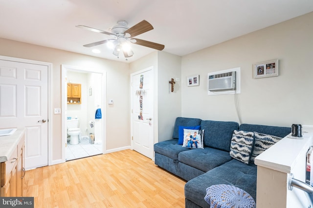 living area featuring a wall mounted air conditioner, light wood-type flooring, baseboards, and ceiling fan