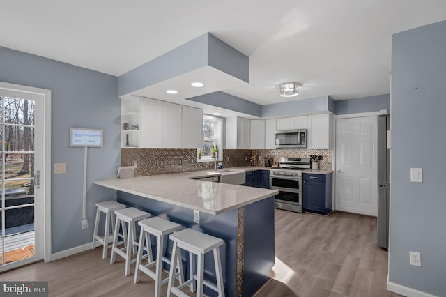 kitchen with decorative backsplash, white cabinets, appliances with stainless steel finishes, and a peninsula