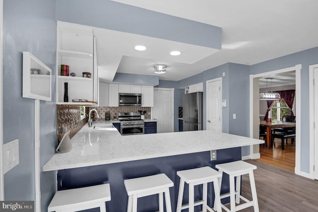 kitchen featuring wood finished floors, a peninsula, stainless steel appliances, decorative backsplash, and white cabinetry