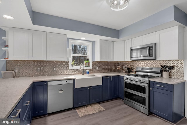 kitchen with blue cabinetry, white cabinets, appliances with stainless steel finishes, and a sink