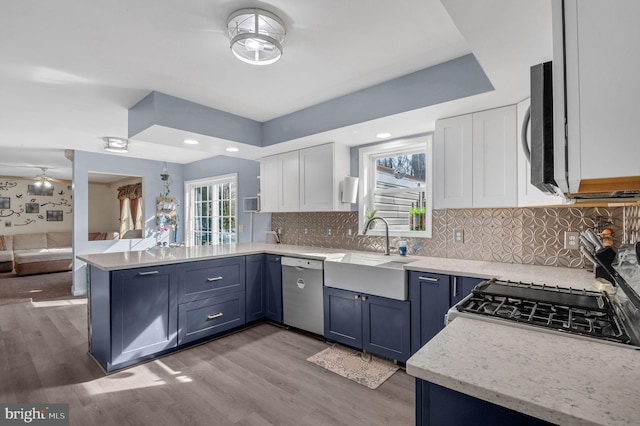 kitchen featuring white cabinetry, a peninsula, a sink, dishwasher, and light wood-type flooring