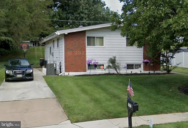 view of home's exterior featuring brick siding, central AC unit, concrete driveway, and a yard