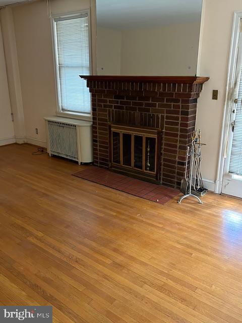 unfurnished living room with a brick fireplace, radiator, wood finished floors, and baseboards