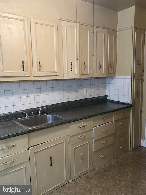 kitchen with a sink, decorative backsplash, dark countertops, and white cabinets