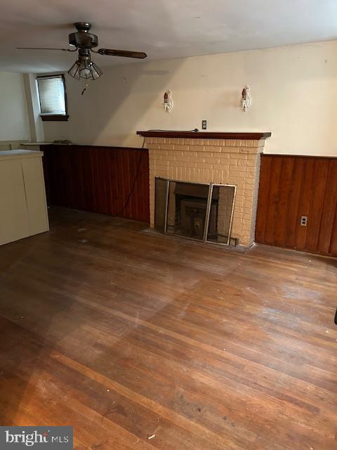 unfurnished living room with wood walls, a brick fireplace, ceiling fan, and wood finished floors