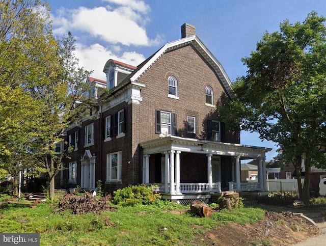 view of front of home with brick siding, a porch, and a chimney