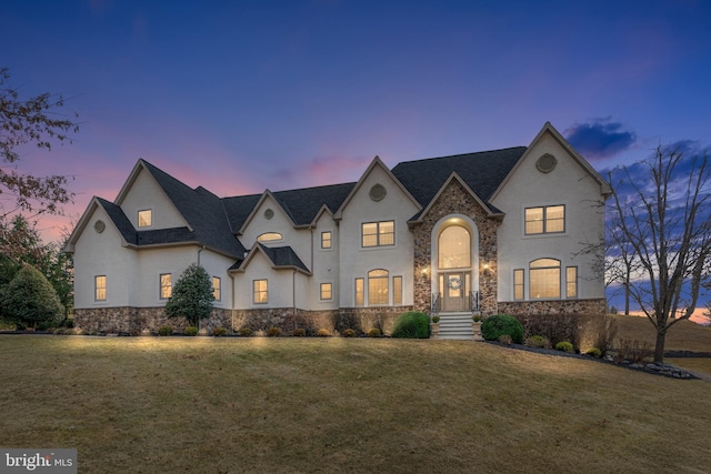 french country home with stone siding, stucco siding, and a front lawn