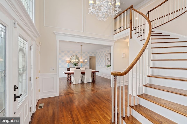 foyer featuring visible vents, a notable chandelier, ornamental molding, a decorative wall, and stairs