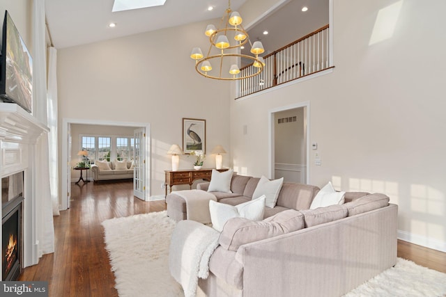 living room with visible vents, a chandelier, a warm lit fireplace, a skylight, and wood finished floors