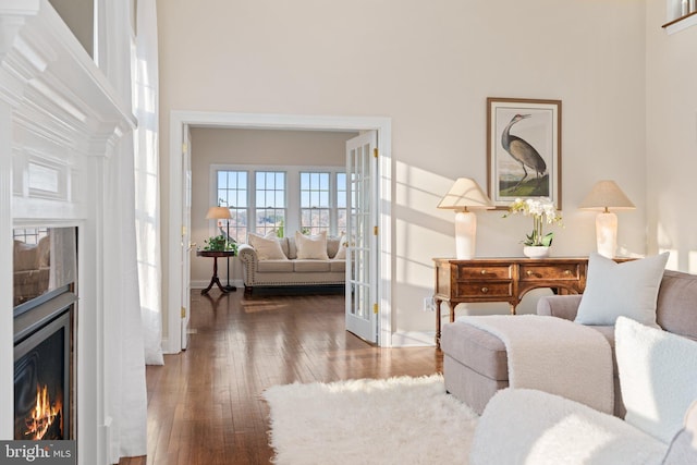 living area with a tiled fireplace, a towering ceiling, baseboards, and wood-type flooring