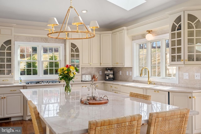 kitchen featuring backsplash, glass insert cabinets, a chandelier, a skylight, and a sink