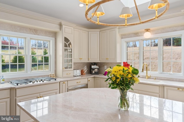 kitchen featuring tasteful backsplash, light stone countertops, stainless steel gas cooktop, a notable chandelier, and a sink