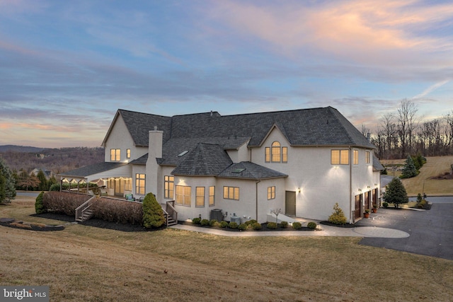 view of front of house with a shingled roof, stucco siding, a yard, a garage, and driveway