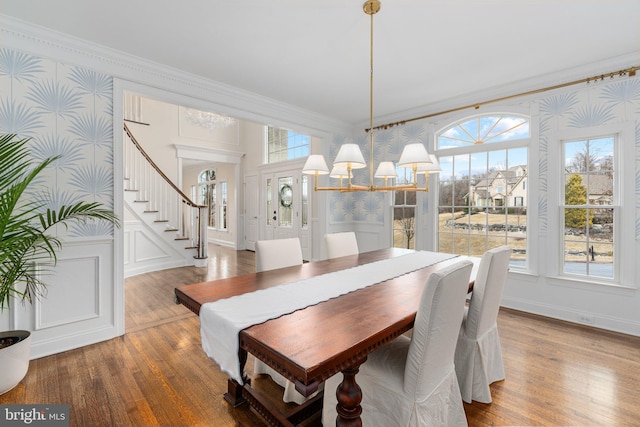 dining space with ornamental molding, wood finished floors, wallpapered walls, a healthy amount of sunlight, and a chandelier