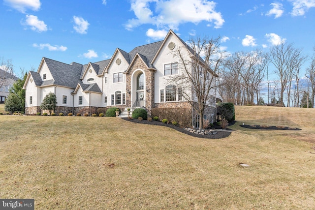 french country inspired facade featuring a front lawn, stone siding, and stucco siding