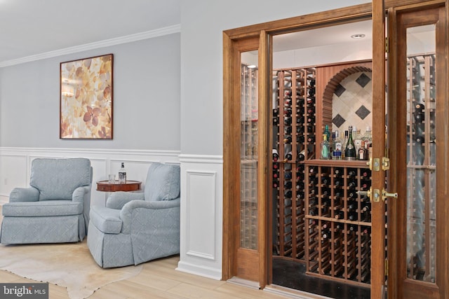 wine area with a decorative wall, wainscoting, wood finished floors, and ornamental molding