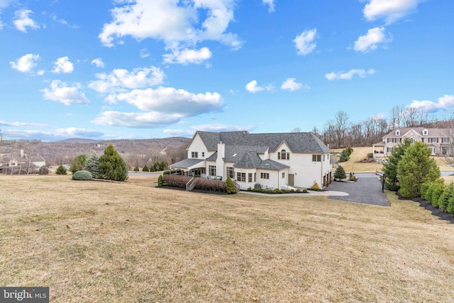 rear view of property featuring a lawn, a mountain view, and driveway