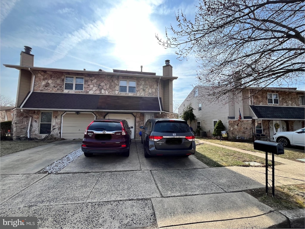 view of front facade with a garage, stone siding, driveway, and a chimney