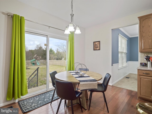 dining space with baseboards, dark wood-type flooring, an inviting chandelier, and ornamental molding