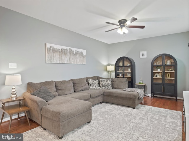 living area featuring built in shelves, baseboards, a ceiling fan, and wood finished floors