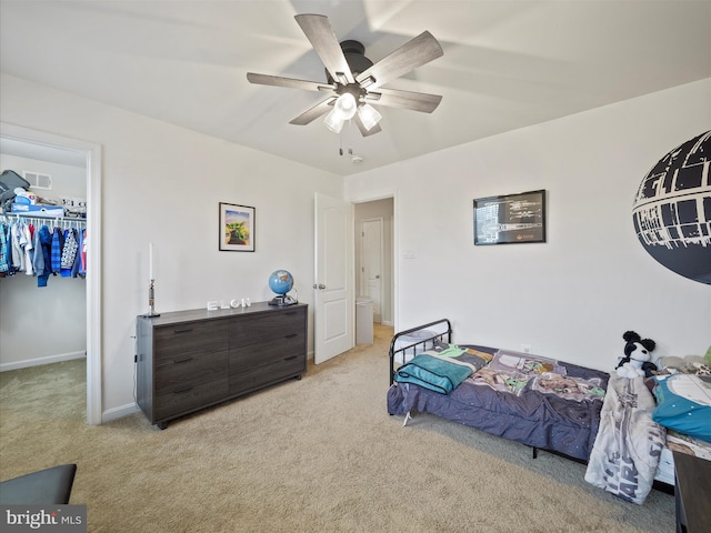 bedroom with a spacious closet, light colored carpet, baseboards, and a ceiling fan