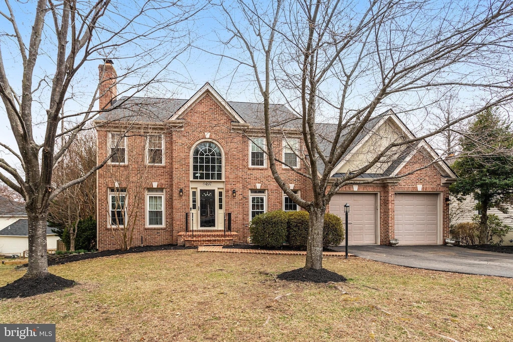 colonial-style house with a chimney, a front lawn, a garage, aphalt driveway, and brick siding