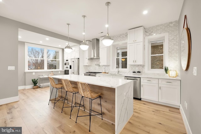 kitchen featuring stainless steel appliances, white cabinets, a center island, and wall chimney range hood