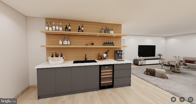 bar featuring beverage cooler, a sink, light wood finished floors, indoor wet bar, and baseboards