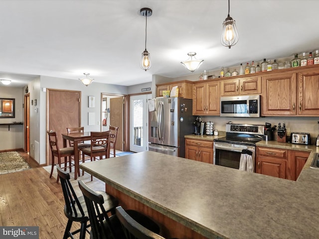 kitchen with a breakfast bar area, light wood finished floors, a peninsula, appliances with stainless steel finishes, and pendant lighting