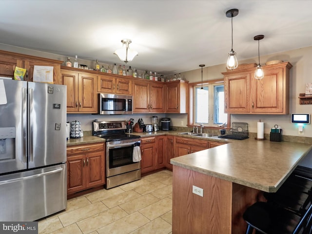 kitchen featuring brown cabinets, a breakfast bar, a sink, stainless steel appliances, and a peninsula