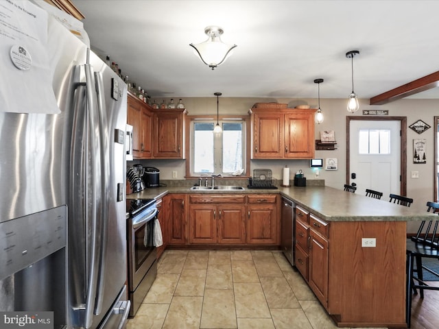 kitchen featuring brown cabinets, a sink, appliances with stainless steel finishes, a breakfast bar area, and a peninsula